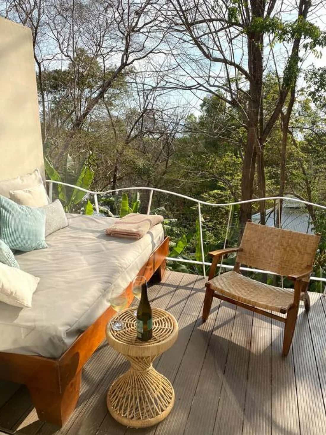 Cama de descanso y sillón de mimbre en una terraza BoHo rodeada de vegetación