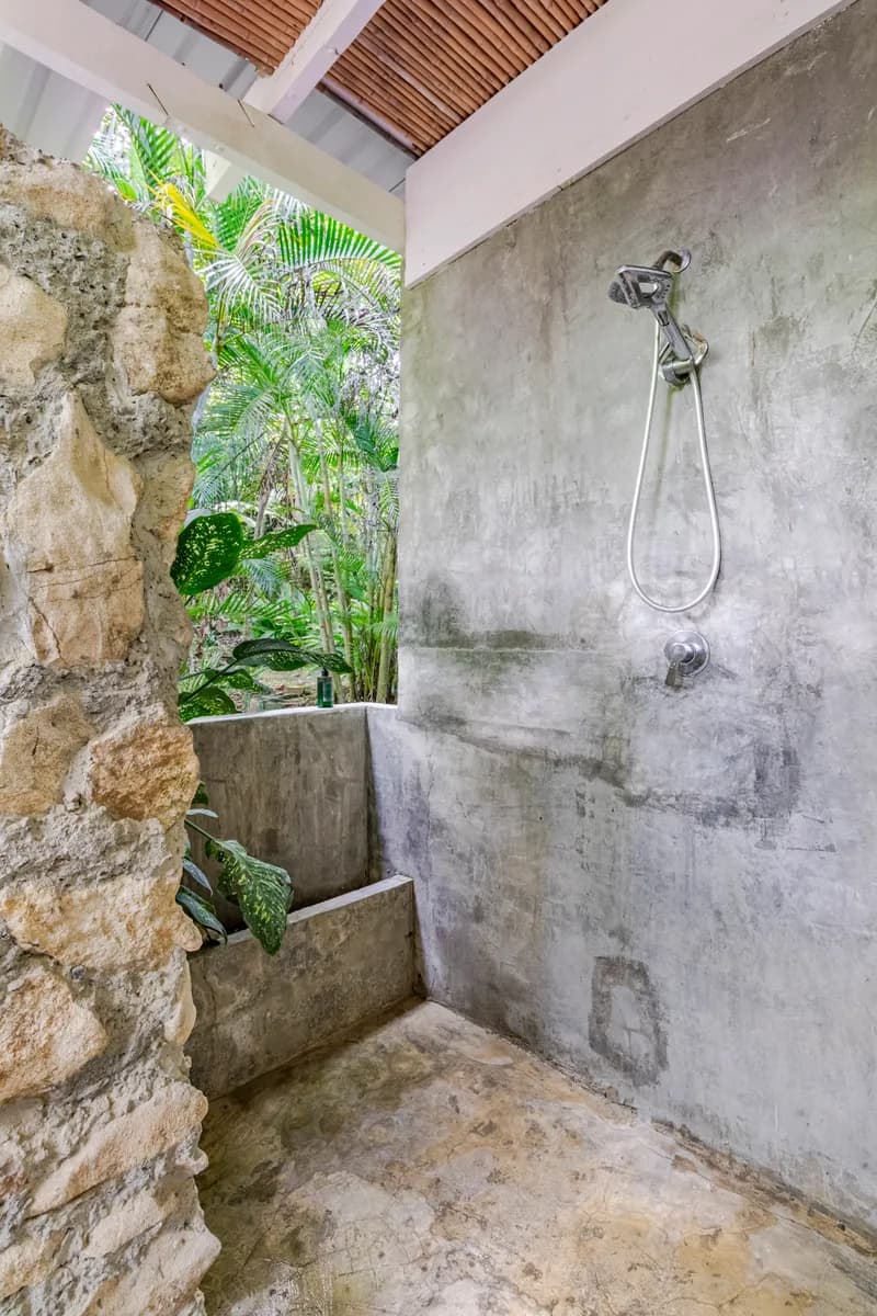 Outdoor shower beside a stone wall and plants — Casa Mapachita